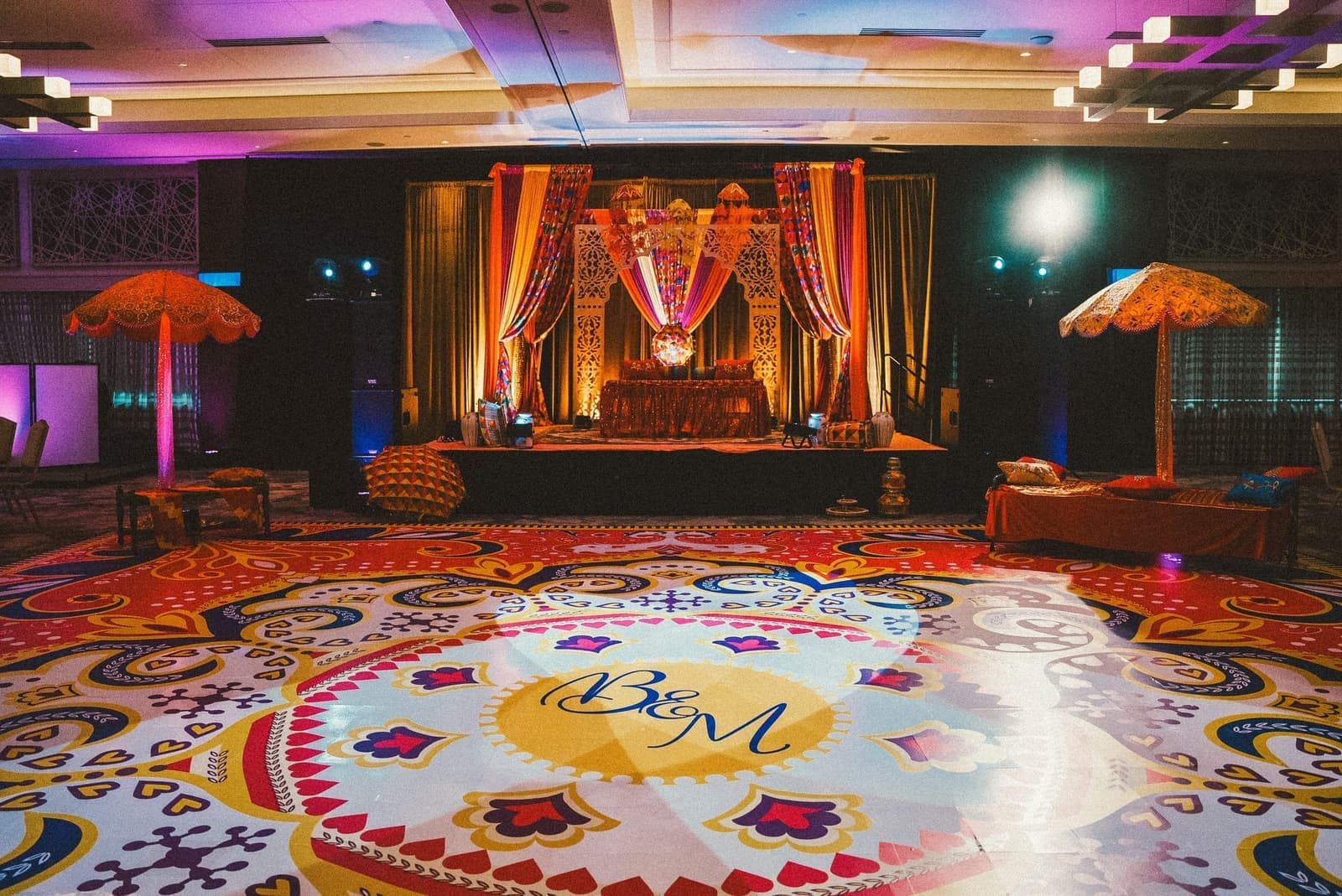 Colorful Mehndi setup with a custom monogram dance floor and ornate stage