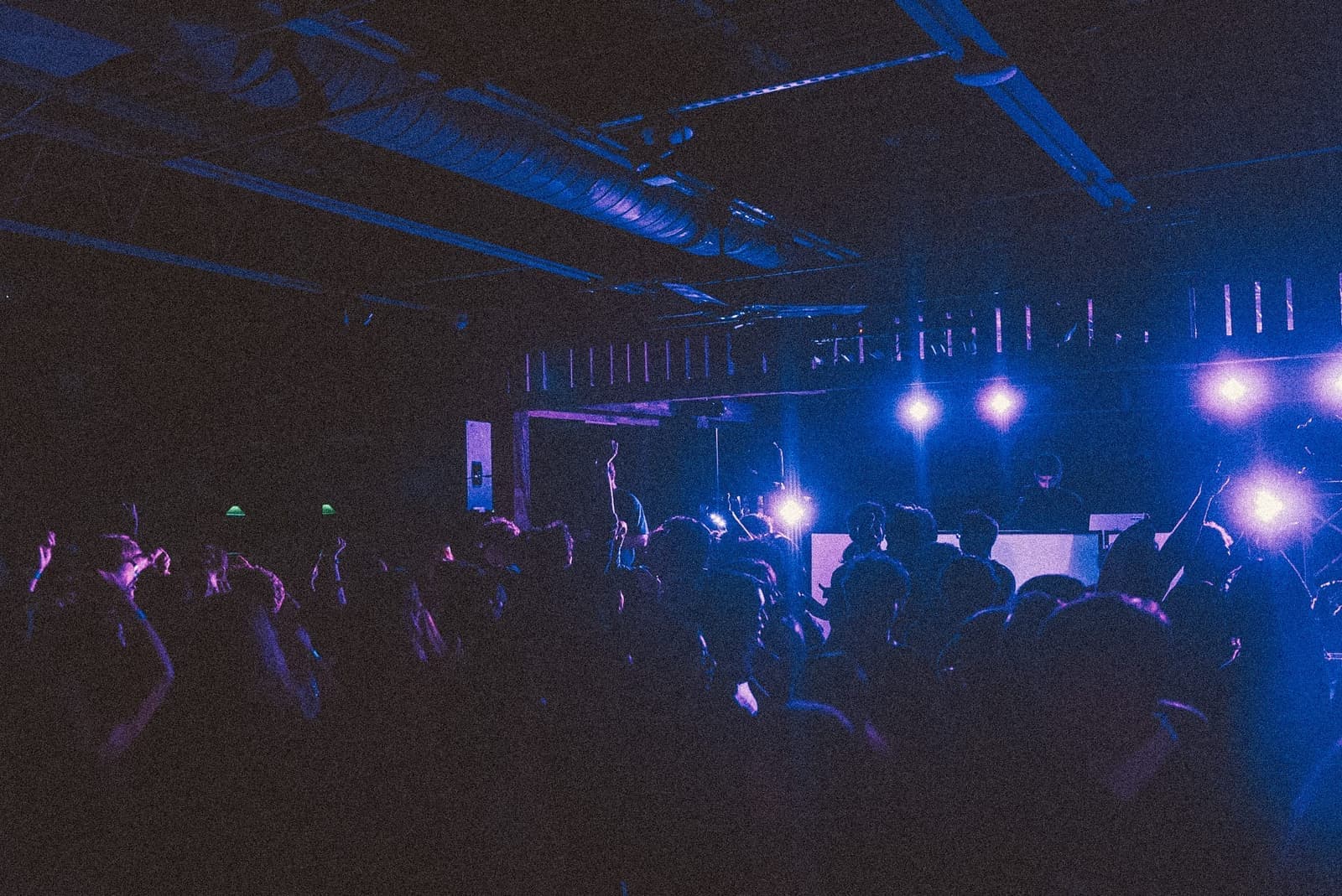 Crowd dancing in front of the DJ booth under blue and purple stage lighting