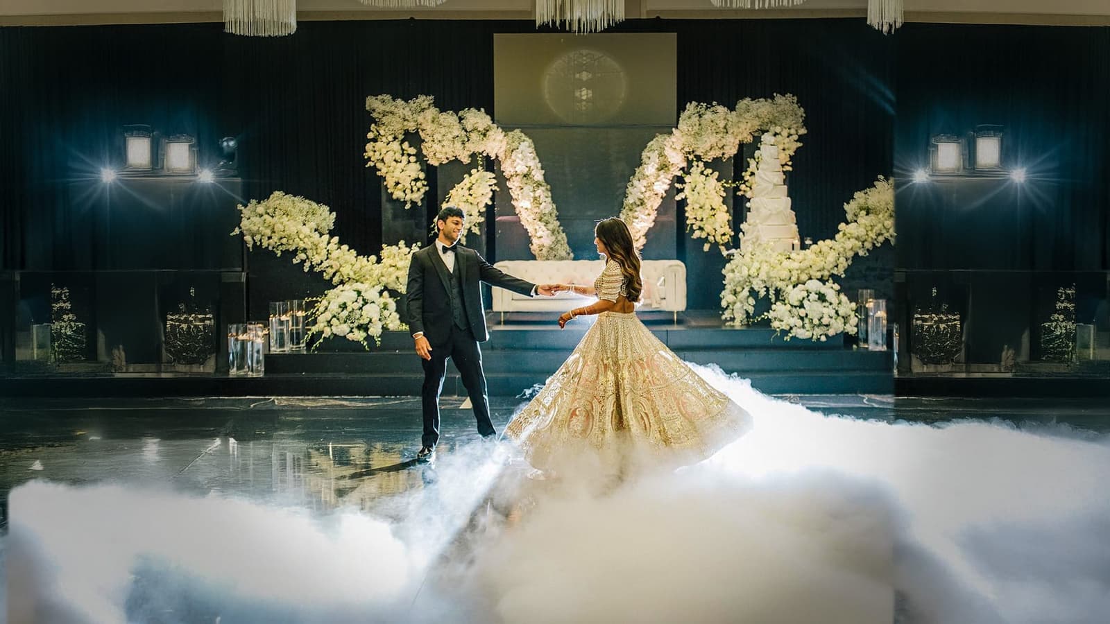 Bride twirling in a gold lehenga with her partner over low-lying fog on the dance floor